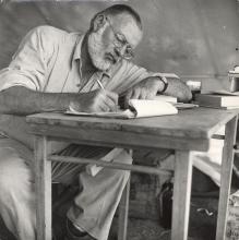 Hemingway writing at a camp table in Africa, 1953-54