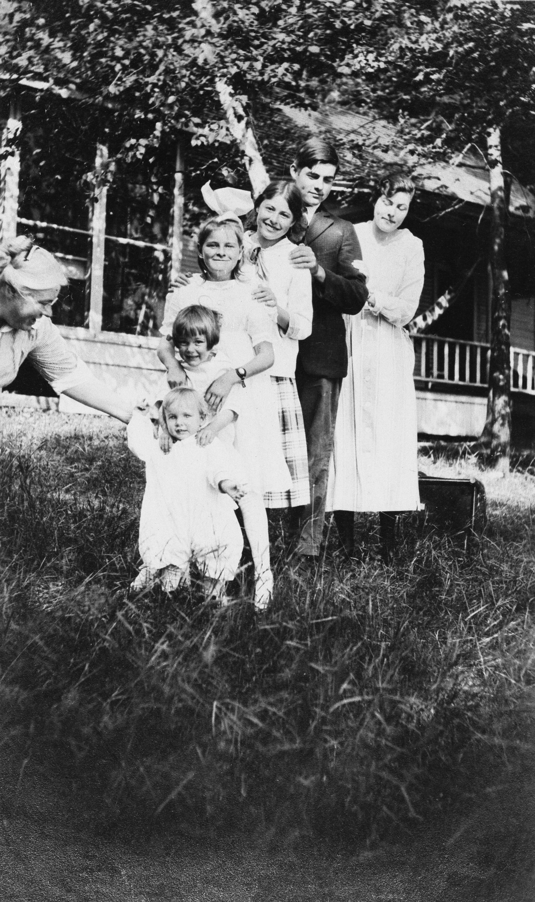The Hemingway siblings lined up in order of age in front of the family's cottage, Windemere, on Walloon Lake, Michigan, 1916.  Their mother, Grace Hall Hemingway, helps steady the baby, Leicester, standing in front of his older siblings.