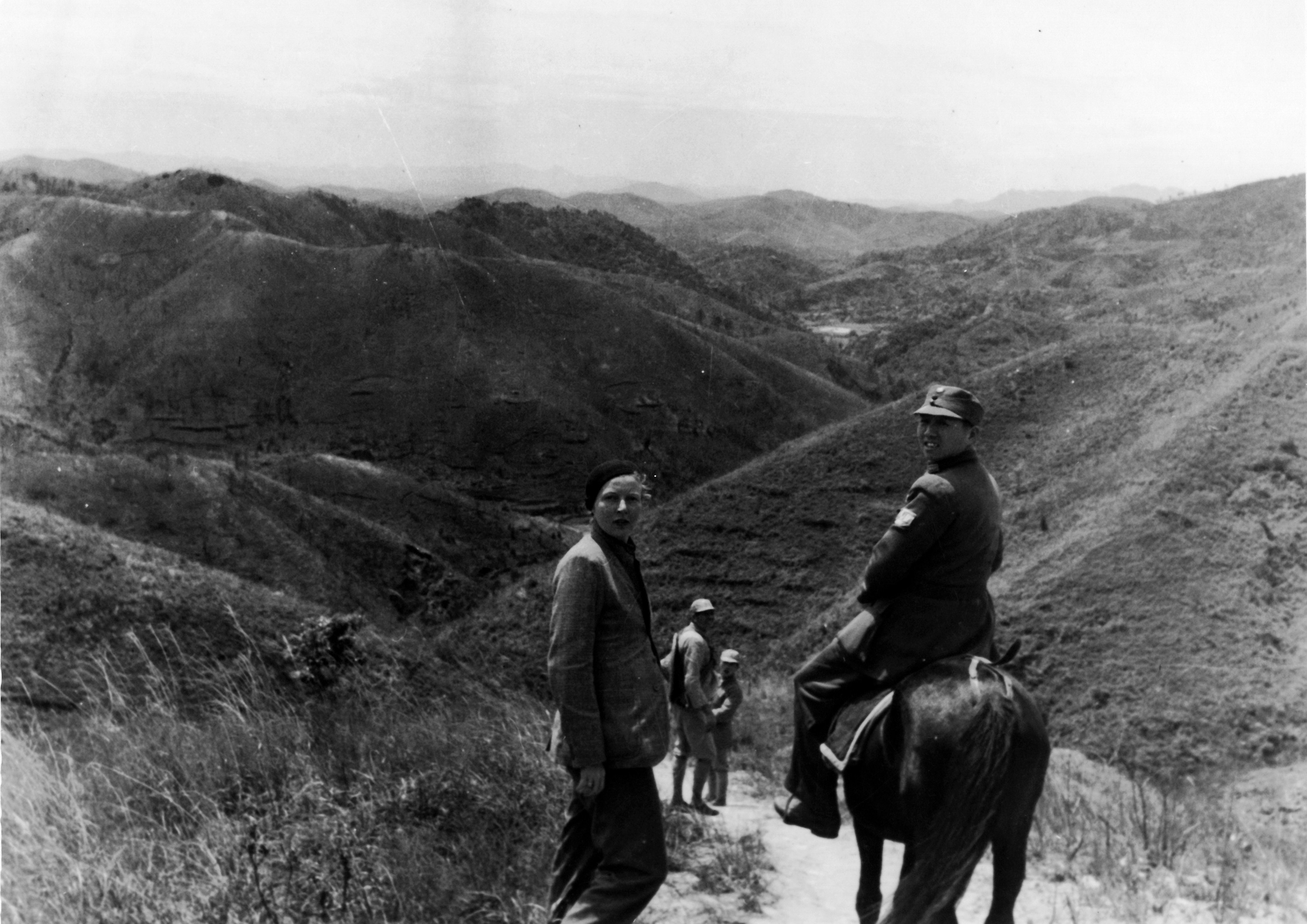 Black and white image of Martha Gellhorn and an unidentified Chinese soldier. The soldier is on horseback; they stand on a mountain trail.