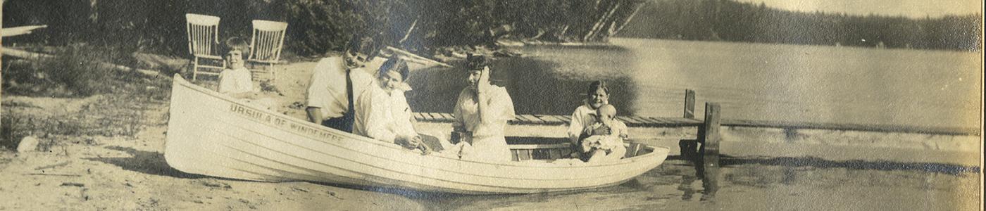 A sepia photograph of Hemingway and his six siblings in the boat "Ursula of Windemere." The boat is pulled up on the sandy shore of Walloon Lake.