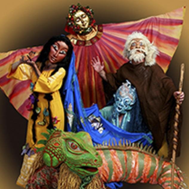 A portrait of four masked characters. A woman in a yellow dress with long hair, the sun with a golden face and shining robe, a village elder in a brown tunic with a wooden staff, the river in a blue mask and cape, and an iguana with green and orange reptile costume.