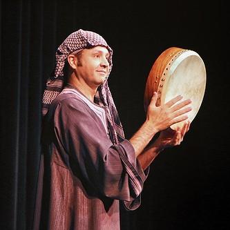 Karim Nagi performing with a hand drum in traditional Arab attire.