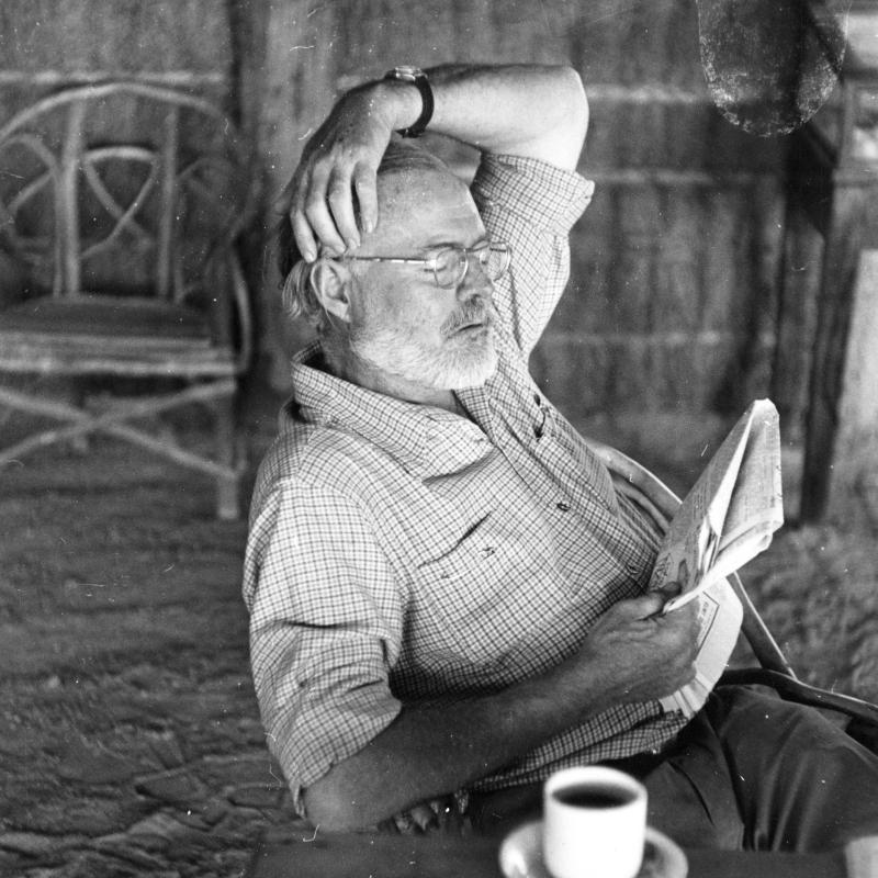 Hemingway reading a newspaper at his camp in Africa, c. 1953.